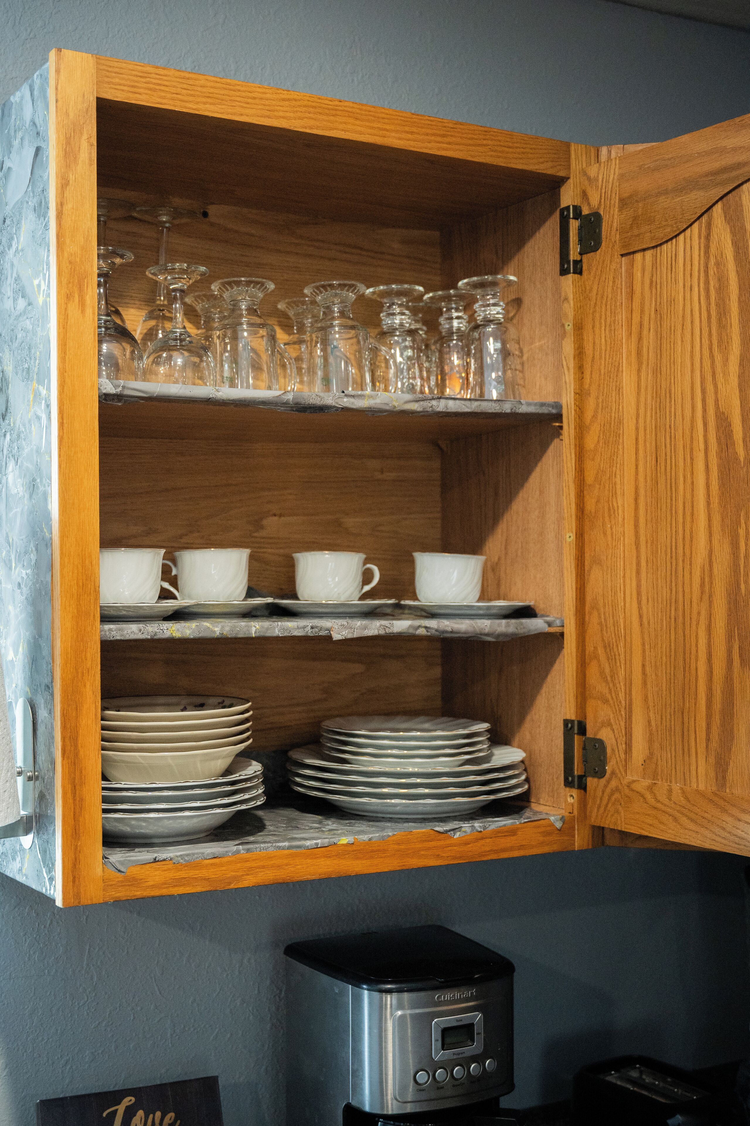 A wooden cabinet with shelves containing glassware, white cups, and stacked plates.