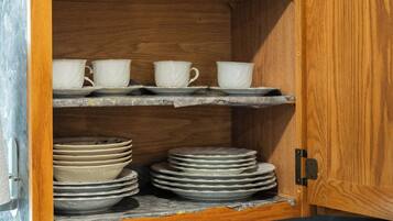 A wooden cabinet with shelves containing glassware, white cups, and stacked plates.