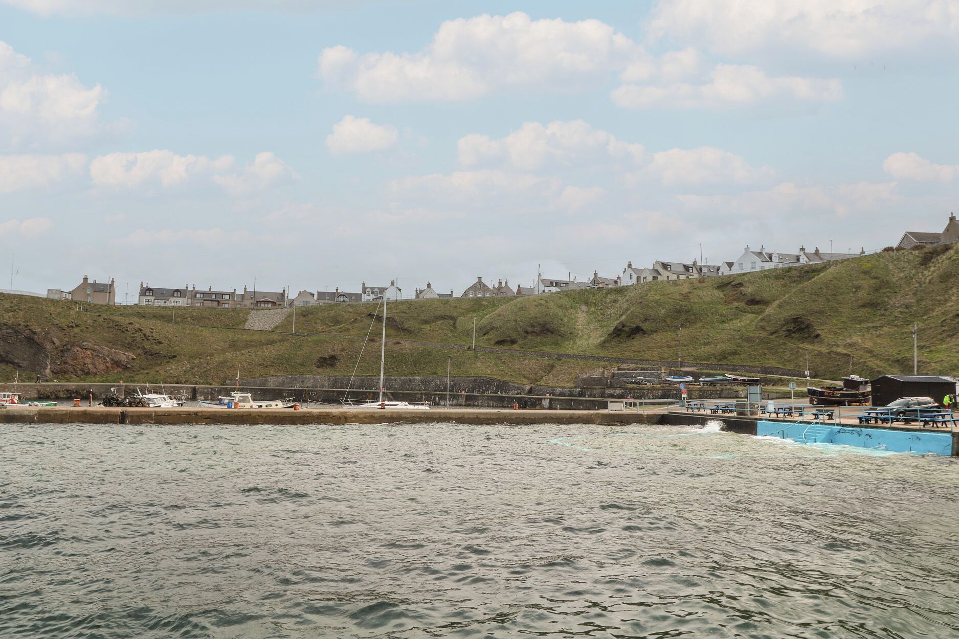 A coastal town with a harbor, boats, and houses on a hillside.