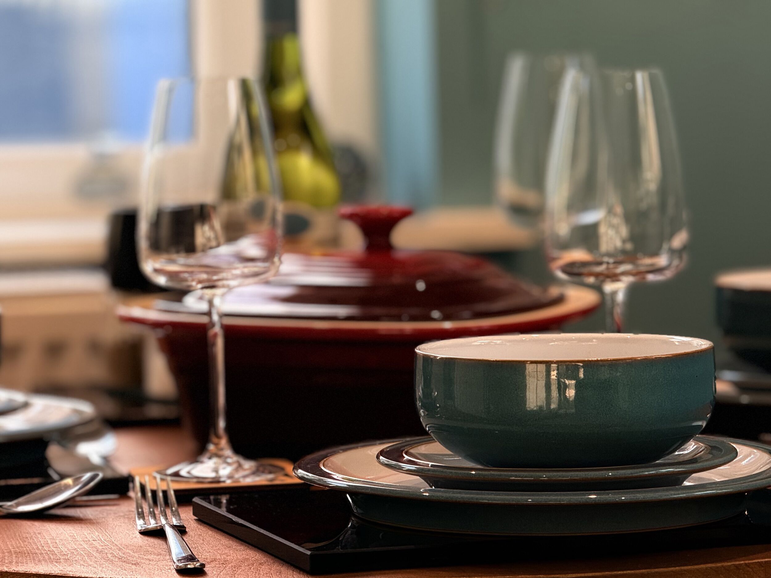 A dining table with a blue bowl, wine glasses, and cutlery.