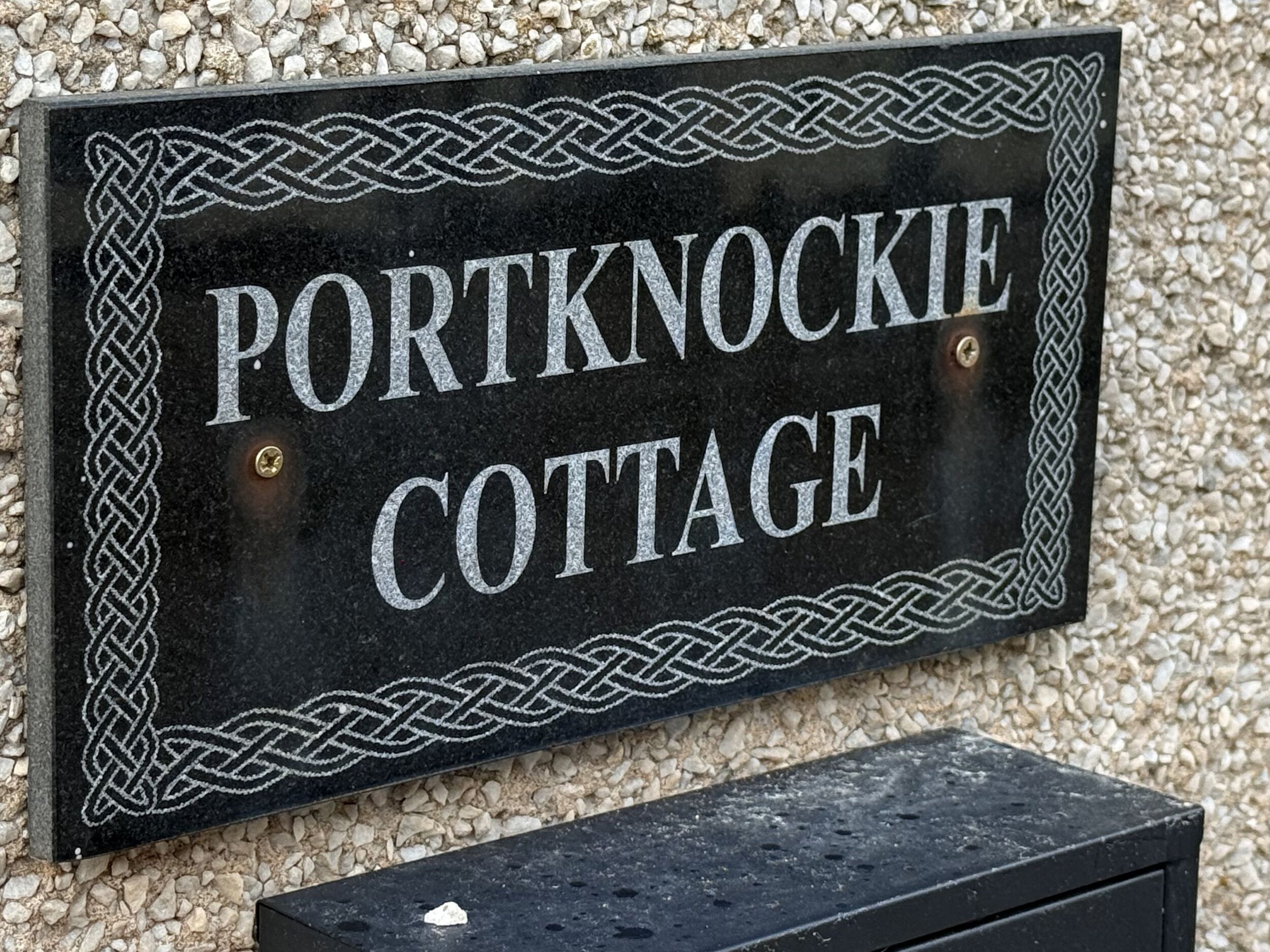 Un panneau indiquant l’emplacement de la maison de vacances « Portknockie Cottage », agrémenté d’une bordure décorative.