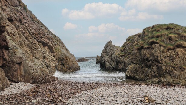 Paesaggio costiero roccioso con spiaggia di ciottoli e scogliere.