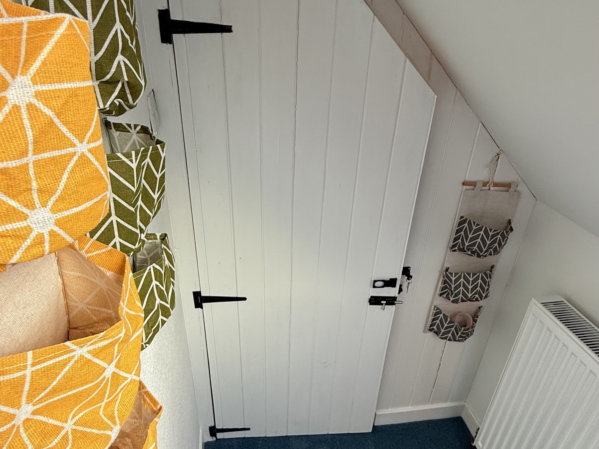 A bedroom with a white wardrobe, a bed with orange and green patterned bedding, and a radiator on the wall.