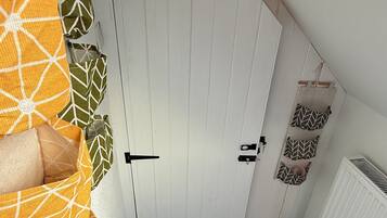 A bedroom with a white wardrobe, a bed with orange and green patterned bedding, and a radiator on the wall.