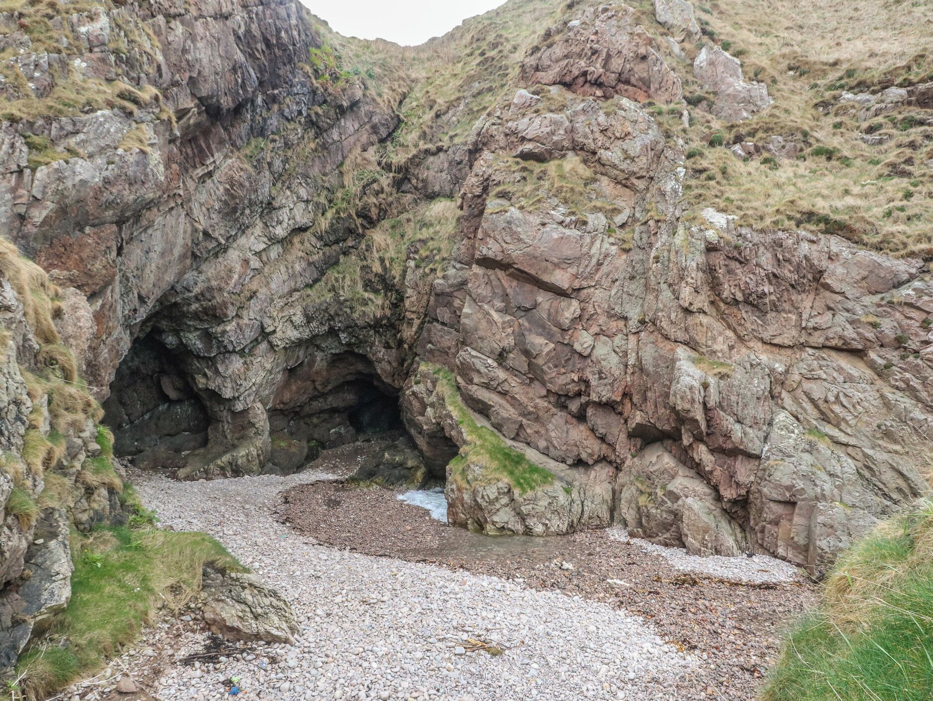 L’entrée d’une grotte rocheuse, avec un sentier de gravier qui la traverse.