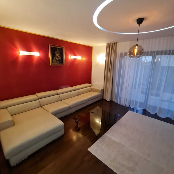A modern living room with a beige sofa, a glass coffee table, and a red accent wall.