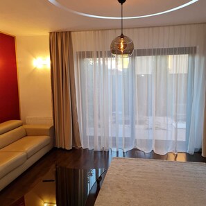 A modern hotel room with a leather sofa, a round table, sheer curtains, and a hanging light fixture.