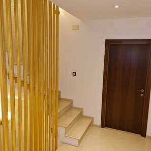 A staircase with beige steps leading to a landing, a wooden door, and a wall-mounted light fixture.