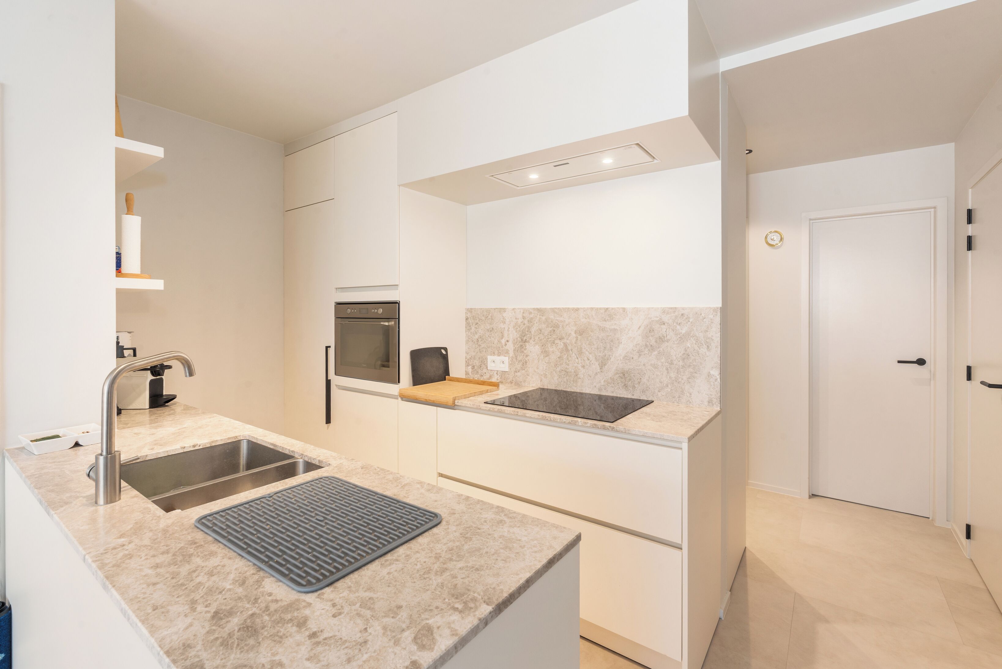 A modern kitchen with a double sink, a built-in oven, and a countertop with a mat.