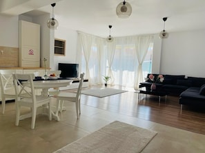 A modern living room with a dining area, a black sofa, and a TV.