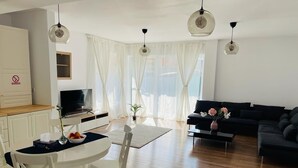 A modern living room with a dark sofa, a dining table with chairs, and a TV. - Galaxy Residence Villa (Odăile)