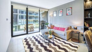 Una sala moderna con un sofá, una mesa de centro y una alfombra. Hay una puerta corrediza de vidrio que da a un balcón con muebles de exterior.