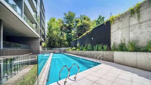 Una piscina moderna al aire libre con agua azul cristalina, rodeada por un muro de hormigón y barandillas de vidrio.