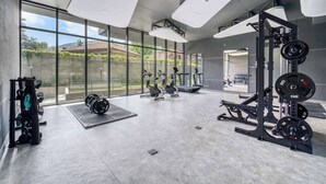 Un gimnasio moderno con diferentes máquinas de ejercicio, ventanas amplias y vistas a zonas verdes.