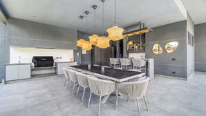 Una cocina moderna con una parrilla empotrada, un comedor con una mesa grande y sillas, e iluminación colgante.