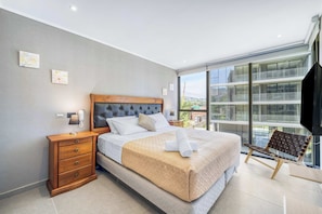 A modern bedroom with a large bed, wooden nightstands, a chair, and a balcony with a view.