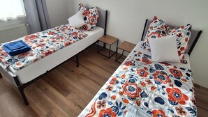 A room with two single beds, each with a floral-patterned bedspread and matching pillows. There is a small wooden table between the beds, and the room has a wooden floor. - Modern & bright 3-room apartment | Wuppertal & Netflix (Wuppertal)