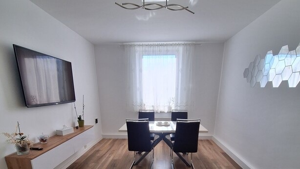 A modern living room with a dining area, wooden flooring, a mounted TV, and a yellow sofa. - Modern & bright 3-room apartment | Wuppertal & Netflix (Wuppertal)