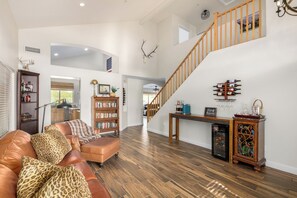 A spacious living room with a high ceiling, a wooden staircase, a fireplace, and a wine rack. - Freedom House: 4BR Pool Home with Mountain Views, Steps from Golf. (Scottsdale)
