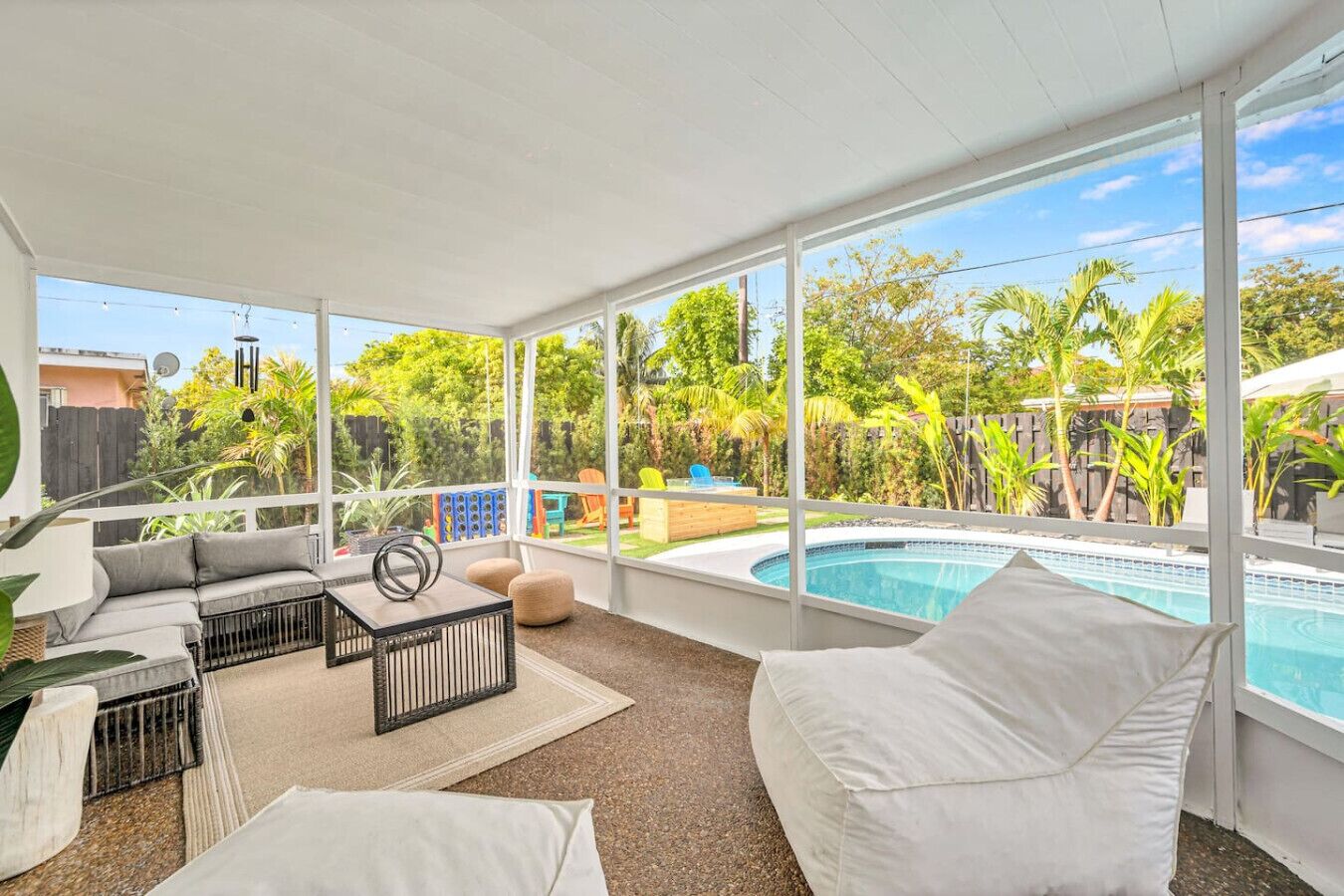 A sunlit patio with a pool, outdoor seating, and a view of a lush garden.