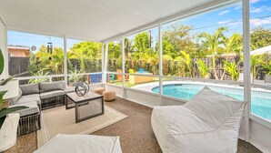 Um pátio ensolarado com piscina, área de estar externa e vista para um jardim exuberante.
