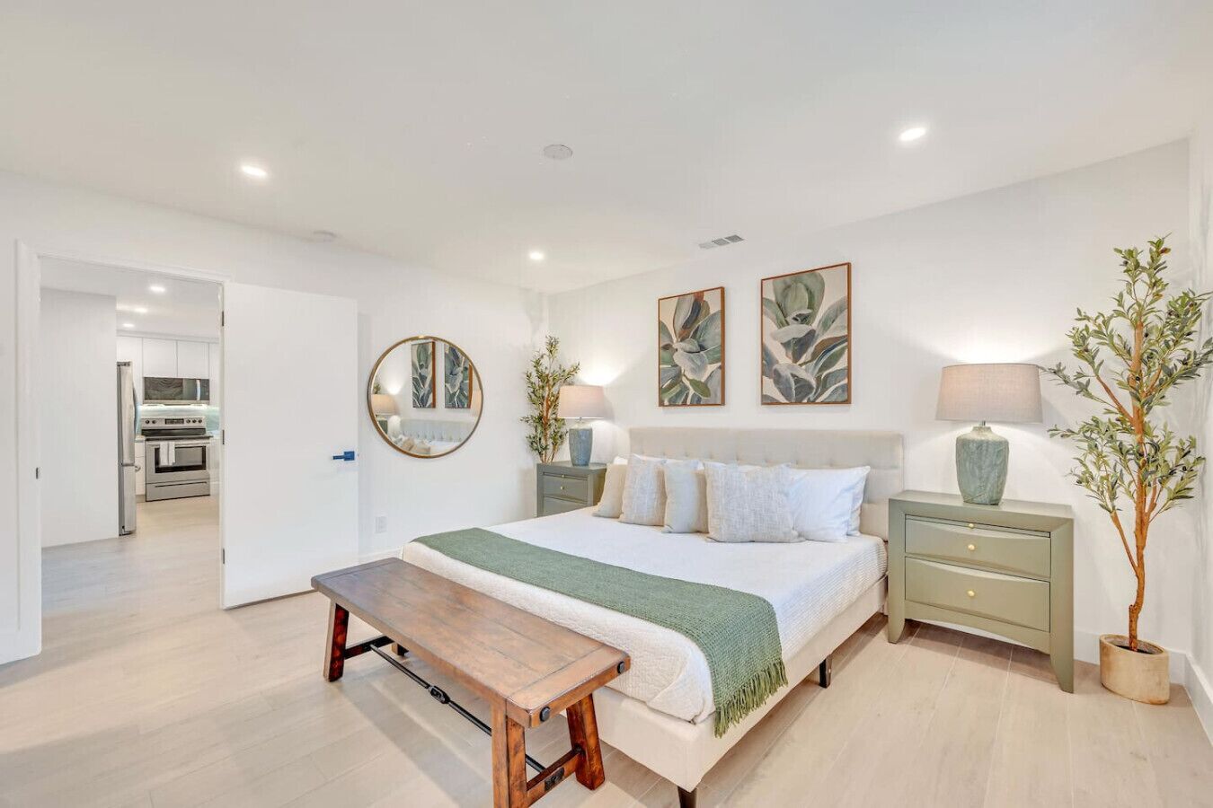 A bedroom with a bed, bedside tables, a bench, a mirror, and artwork on the wall.