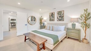 Um quarto com cama, mesas de cabeceira, um banco, um espelho e obras de arte na parede.