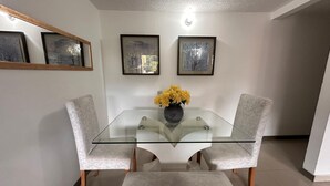 A dining area with a glass table, two cushioned chairs, and a vase of yellow flowers. - View + Swimming Pool Fast WiFi | 100 Meters subway". (Sabaneta)