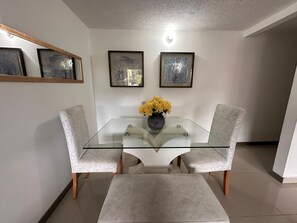 A dining area with a glass table, two cushioned chairs, and a vase of yellow flowers. - View + Swimming Pool Fast WiFi | 100 Meters subway". (Sabaneta)