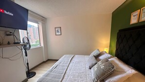A bedroom with a bed, a TV mounted on the wall, a window, and a picture frame. - View + Swimming Pool Fast WiFi | 100 Meters subway". (Sabaneta)