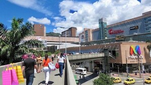 A busy urban scene with a pedestrian walkway, a bridge, and modern buildings including a bank and a store. - View + Swimming Pool Fast WiFi | 100 Meters subway". (Sabaneta)
