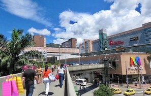 A busy urban scene with a pedestrian walkway, a bridge, and modern buildings including a bank and a store. - View + Swimming Pool Fast WiFi | 100 Meters subway". (Sabaneta)