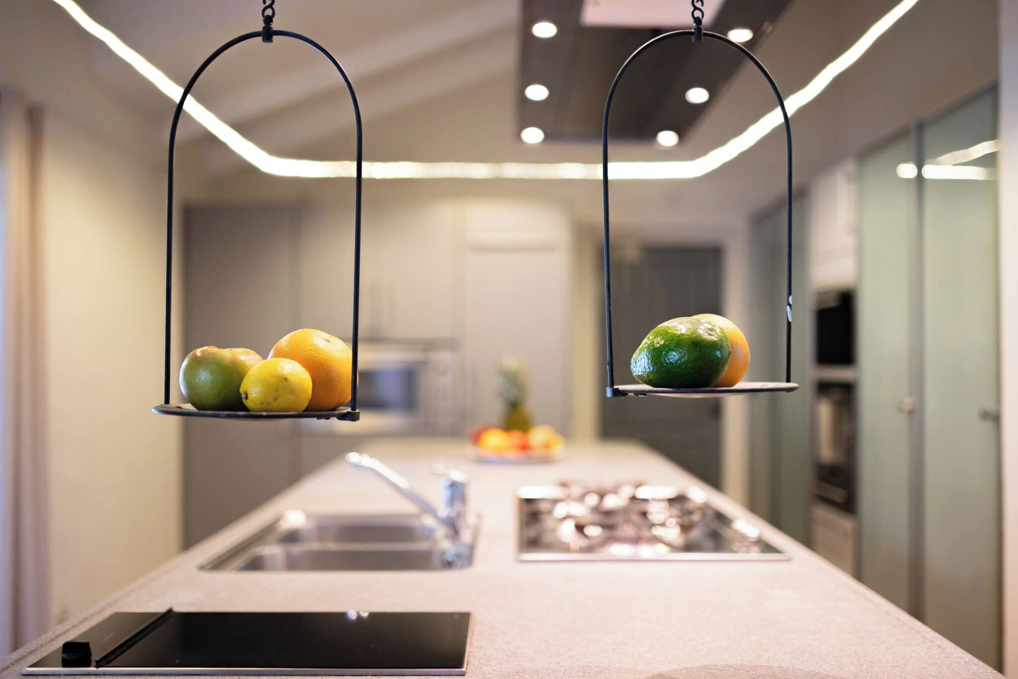 A kitchen with a central island, a sink, and hanging fruit baskets.
