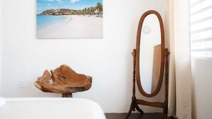 Una habitación con una escultura de madera, una fotografía enmarcada de la playa y un espejo con marco de madera.