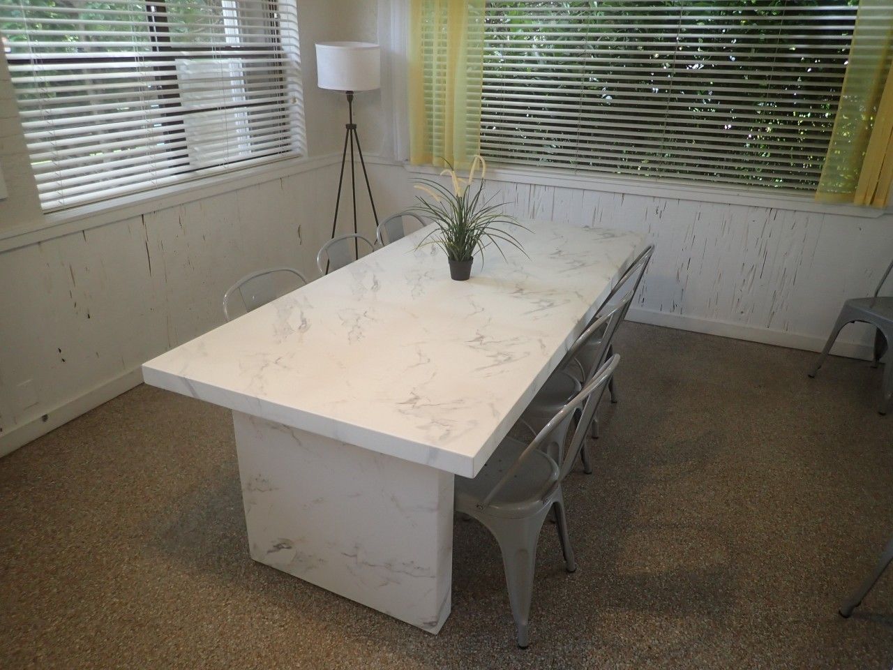 Una habitación con una mesa de mármol, sillas, una planta en maceta y una lámpara.