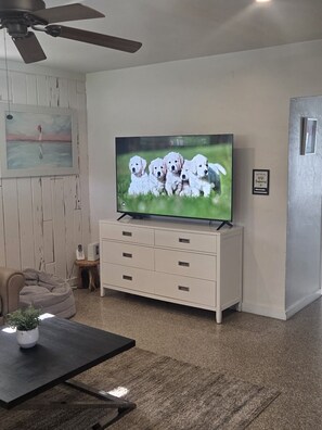 A living room with a television displaying puppies, a ceiling fan, a painting, and a small table with a plant. - 🔥FIFA Home Base with Private Pool🌴 • 2BR/2Bath Family Retreat Sleeps 8 • Near Beach • World Cup Ready • 3 beds & a sofa bed (Hollywood)