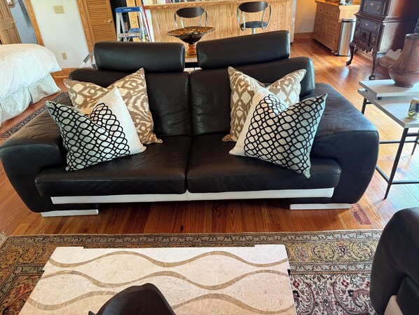 A black leather sofa with patterned cushions, a wooden floor, and a patterned rug.