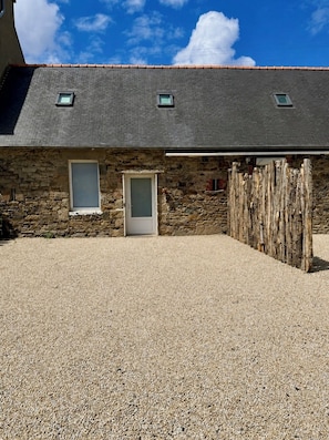 A stone building with a gravel driveway, a wooden fence, and a door. - Cosy house with garden, quiet, near beach & port (paimpol)