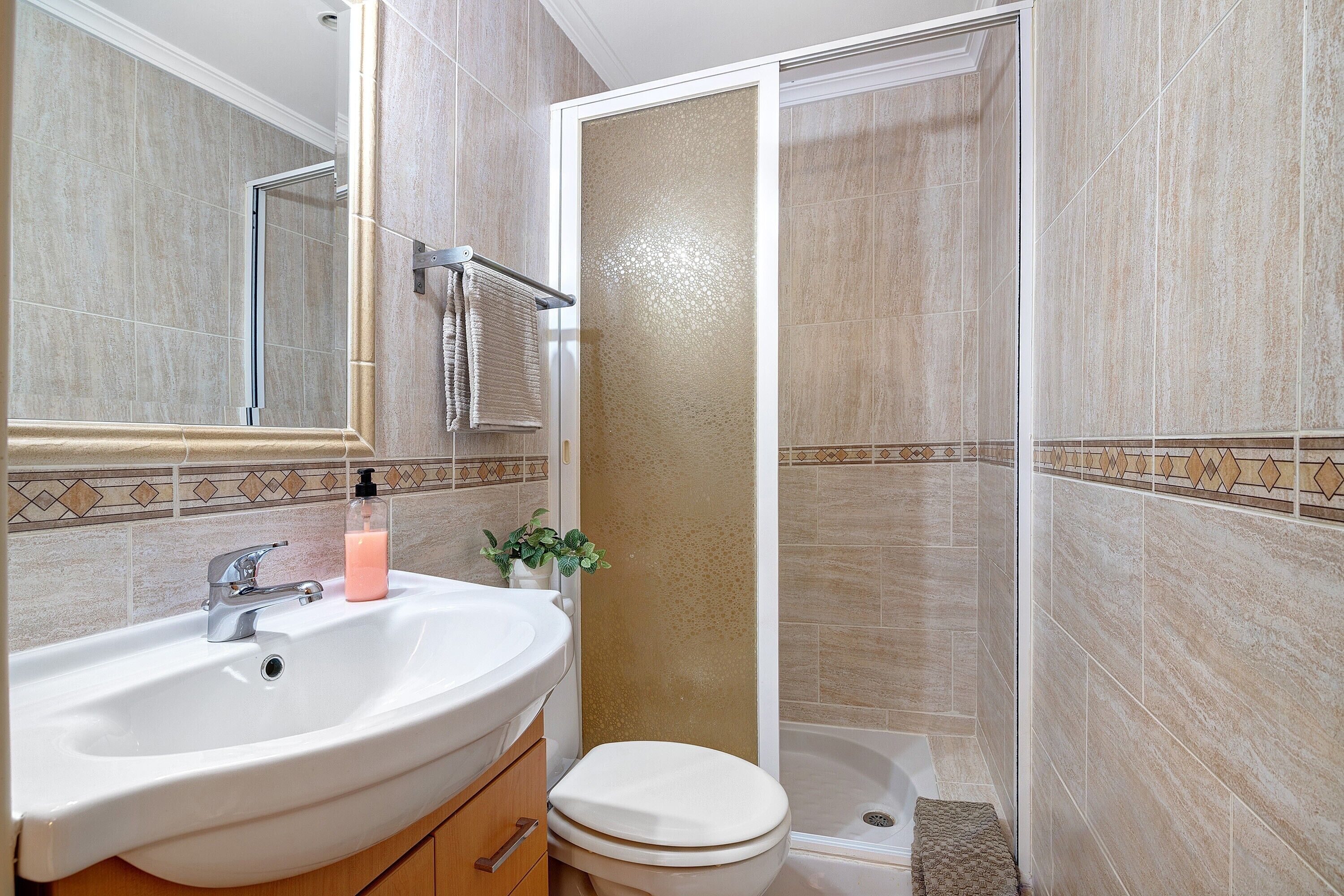 A bathroom with a sink, mirror, toilet, and shower.
