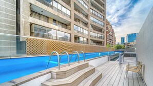 Una piscina sul tetto con gradini che conducono all'acqua, circondata da un pontile in legno e un edificio con balconi.
