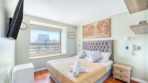 Una camera da letto con un letto grande, una finestra vista città, una TV a parete e un quadro appeso.