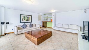 Un soggiorno moderno con un tavolino in legno, due divani bianchi, un'opera d'arte incorniciata e un'area cucina sullo sfondo.