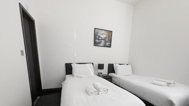 A hotel room with two single beds, a small bedside table with a lamp, and a framed picture on the wall. - Standard Twin Room (Hounslow)