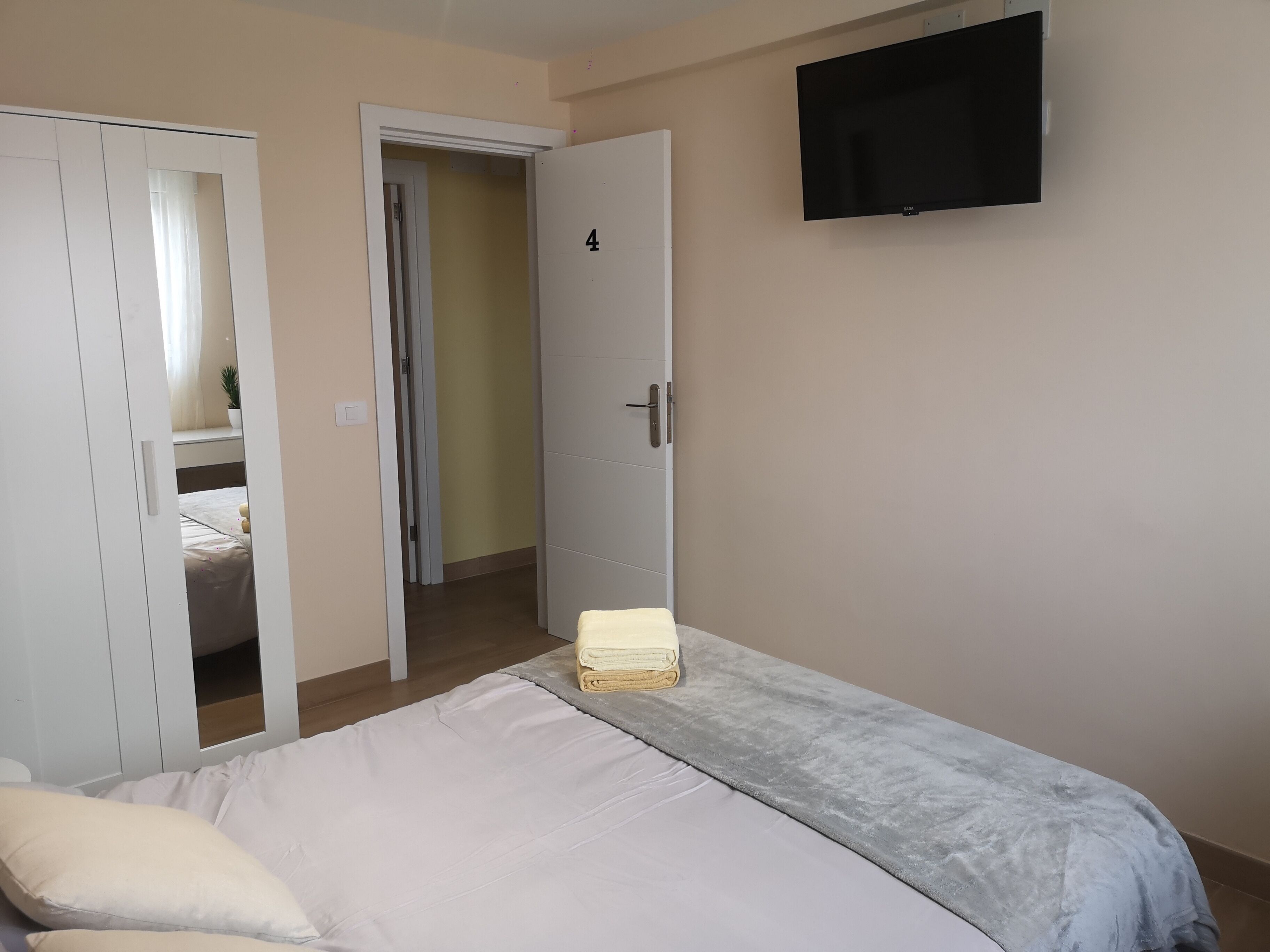 Un dormitorio con cama, televisor montado en la pared y armario.