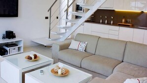 A modern living room with a sofa, coffee table, and a staircase leading to a kitchen area. - Villa Bettina - Charming Interior Spaces (San Jaime Mediterráneo)