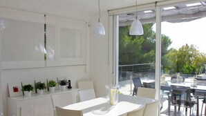 A modern dining area with a white table and chairs, a glass-top table, and a view of the outdoors through large windows. - Villa Bettina - Charming Interior Spaces (San Jaime Mediterráneo)