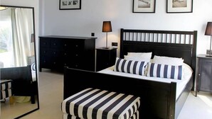 A bedroom with a black and white striped bed, a matching bench, a dresser, and framed pictures on the wall. - Villa Bettina - Charming Interior Spaces (San Jaime Mediterráneo)