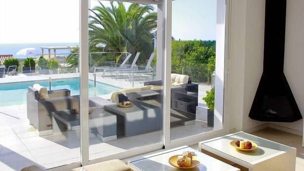 A modern living room with a pool view, featuring a sofa, two coffee tables, and a fireplace. - Villa Bettina - Charming Interior Spaces (San Jaime Mediterráneo)