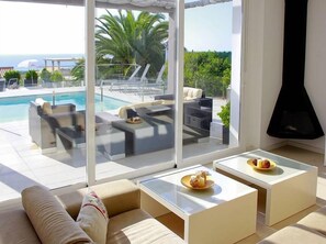A modern living room with a pool view, featuring a sofa, two coffee tables, and a fireplace. - Villa Bettina - Charming Interior Spaces (San Jaime Mediterráneo)