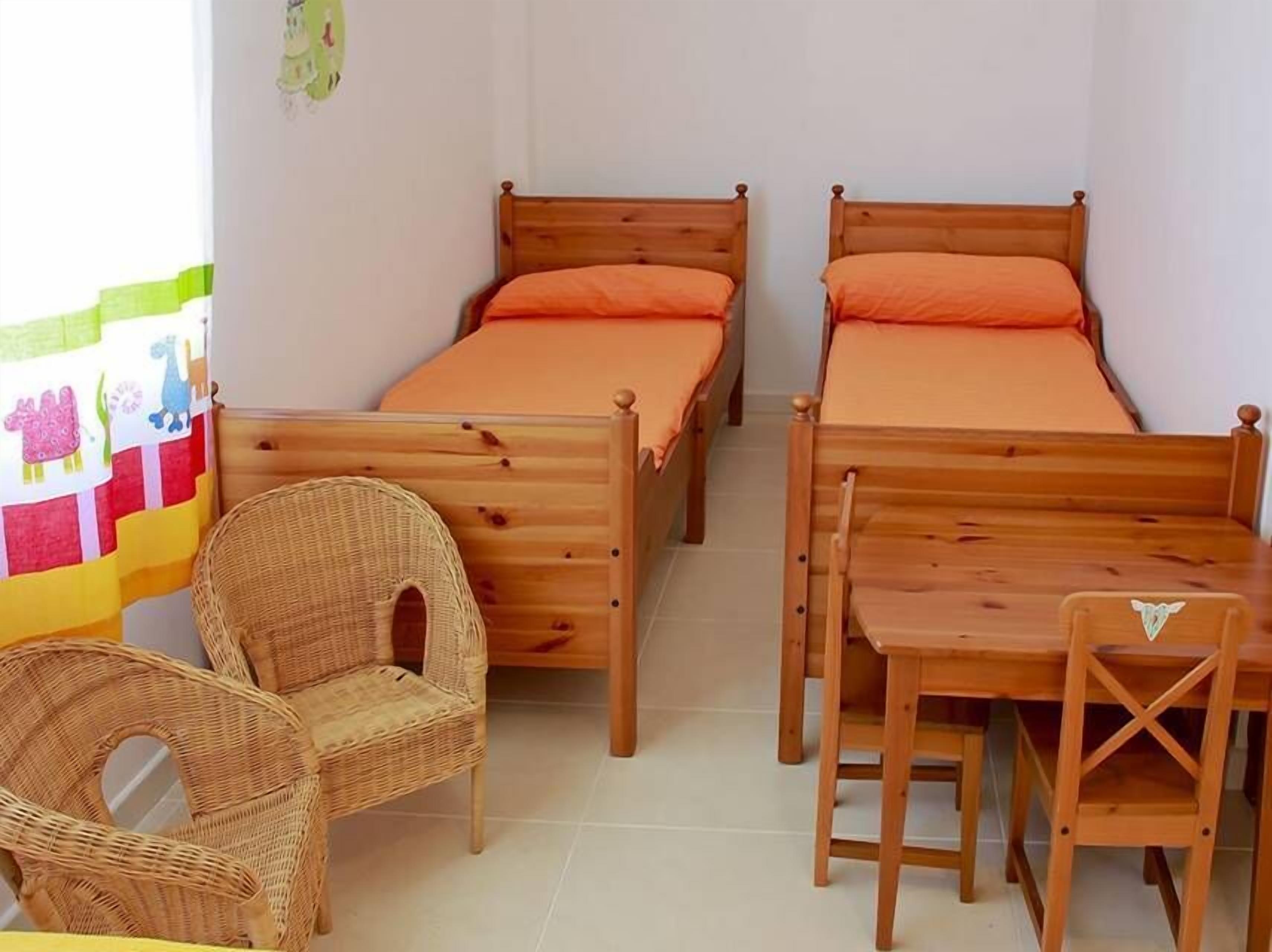 Una habitación con dos camas de madera, una silla de mimbre y una pequeña mesa de madera.